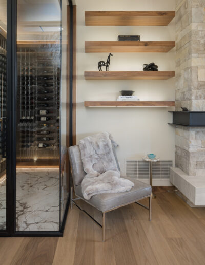 A modern interior featuring a wine cellar, sleek shelves, a cozy chair, and a stylish fireplace, with warm wood flooring.