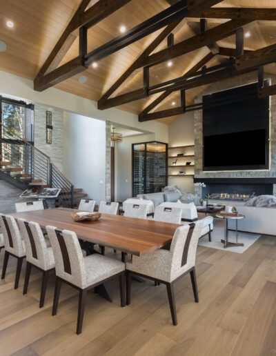 A modern living space featuring high wooden beams, a stylish dining area, and a cozy seating arrangement near a fireplace.