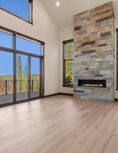 A spacious modern living room featuring tall windows, a stone fireplace, and a view of trees outside.