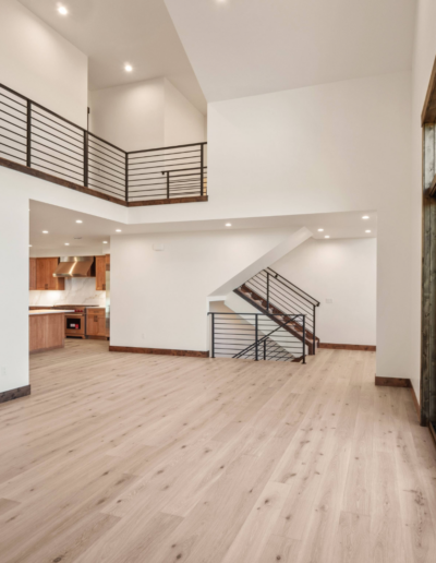 A spacious, modern interior showcasing a wooden floor, an open layout, and contemporary railings leading to a staircase.