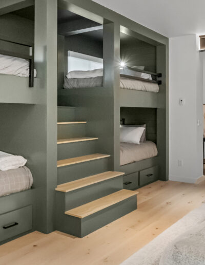 A modern room featuring twin bunk beds in green, wooden floors, and stylish seating, creating a cozy and functional space.