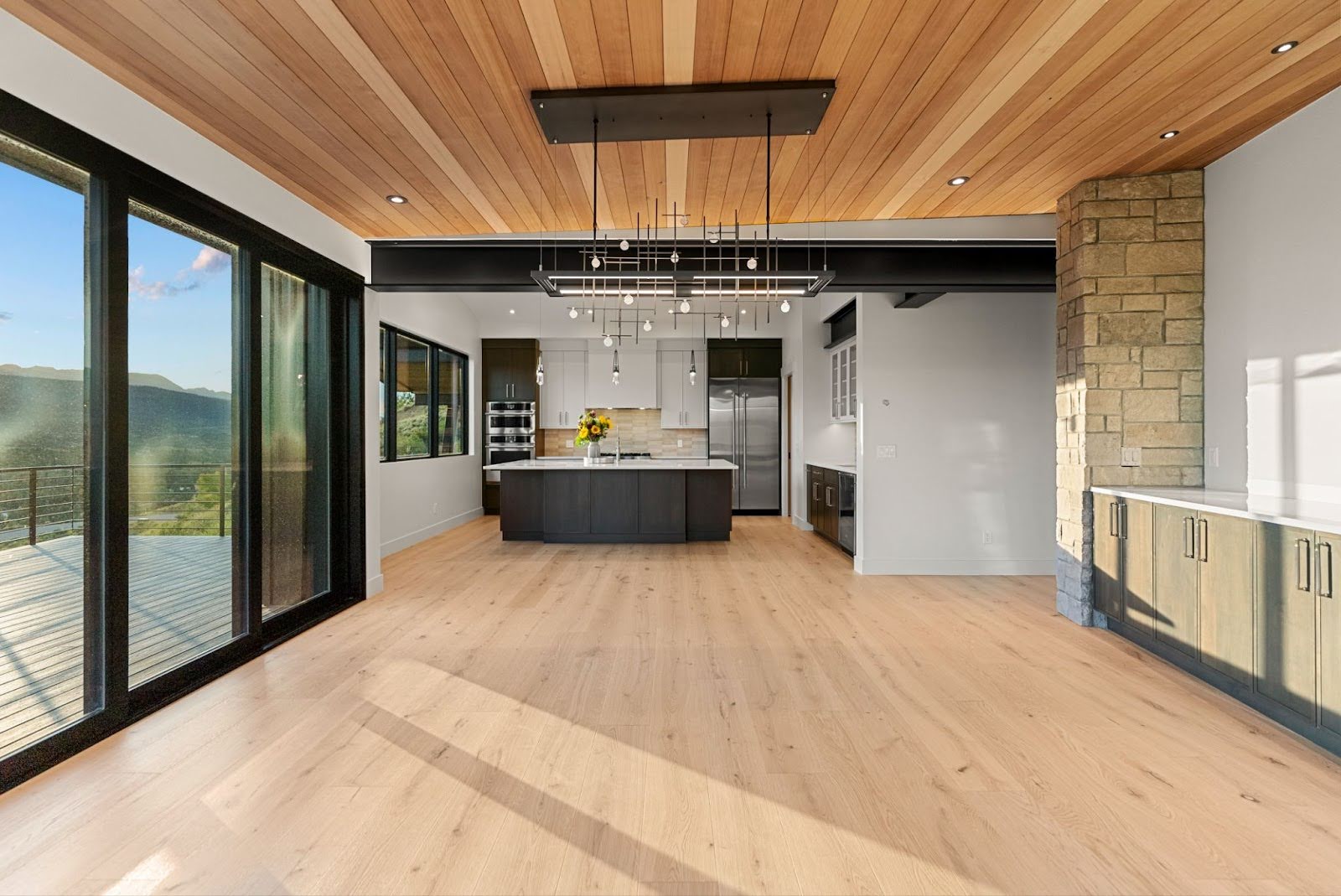 A modern open-concept interior with wooden flooring, large windows, and a contemporary kitchen featuring a central island and stylish lighting.