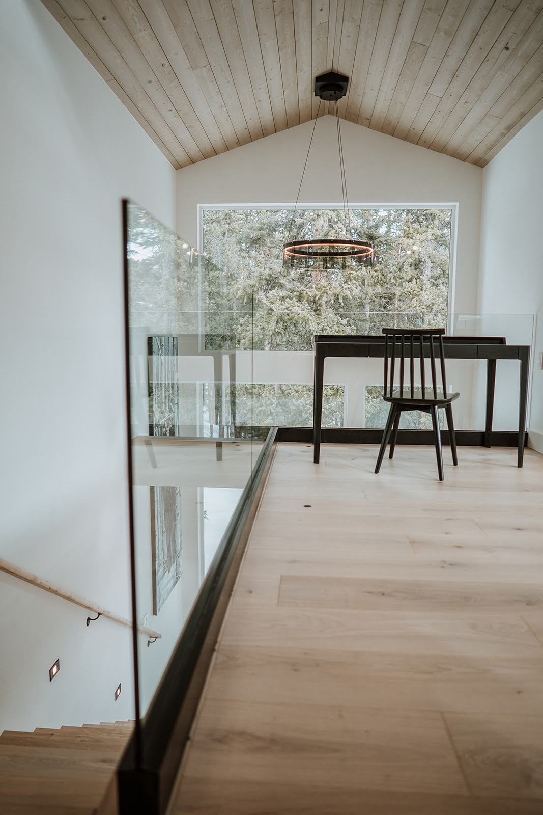 Modern interior featuring a desk and chair overlooking a balcony with large windows, complemented by wooden flooring and ceiling.