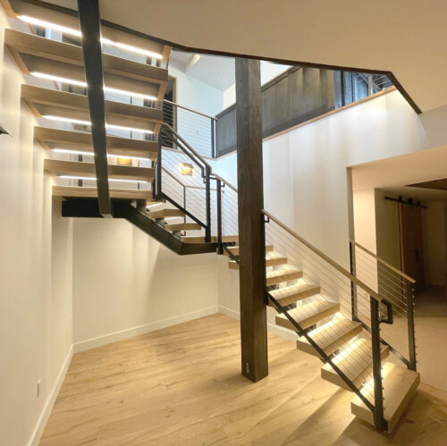 A modern staircase with wooden steps and metal railings, featuring stylish lighting and an open design in a spacious interior.