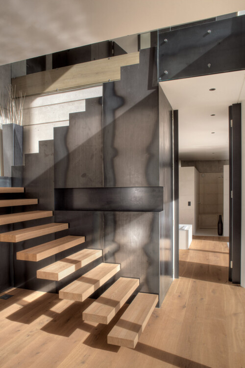A modern interior featuring a sleek staircase, combining wood and metal elements, with natural light highlighting the design.