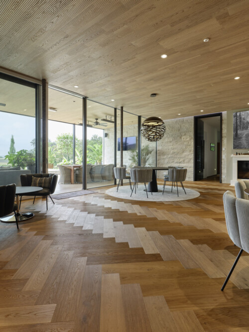 Modern interior space with wooden flooring, stylish furniture, and large windows showcasing greenery outside.