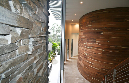 A modern interior featuring a curved wooden wall alongside textured stone, illuminated by warm lighting and showcasing a seamless transition between nature and design.