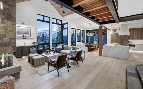 A spacious, modern living area featuring large windows, wooden beams, and stylish furniture, blending comfort with an inviting atmosphere.