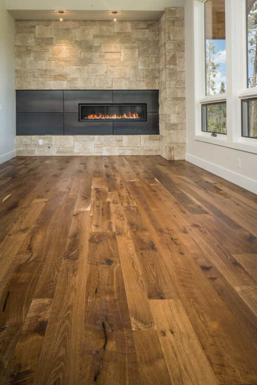 A modern interior with polished wooden flooring, a stylish stone wall, large windows, and a sleek black fireplace.