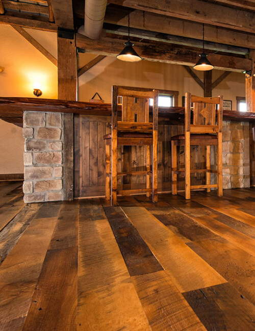 A rustic interior showcasing wooden flooring, a bar with stone accents, and warm lighting, creating a cozy atmosphere.