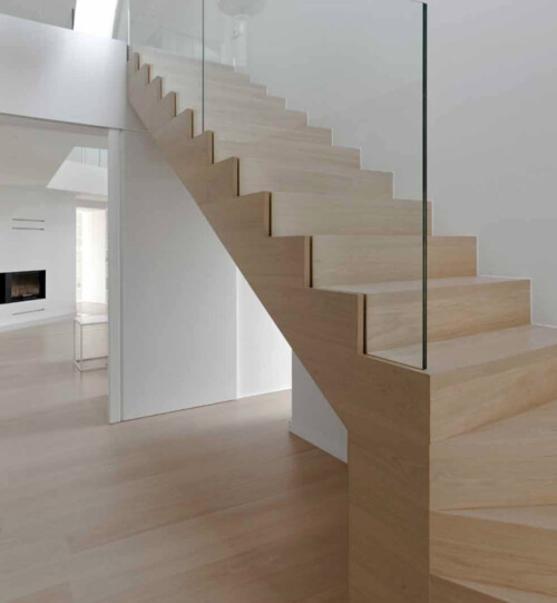 Modern wooden staircase with a minimalist design, featuring glass railings and sleek lines in a spacious interior.
